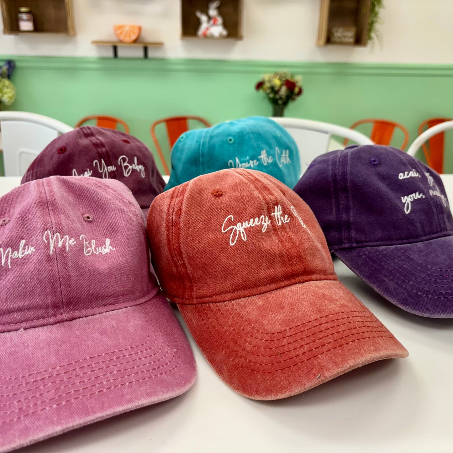 baseball caps in different colors with embroidered text on a table.