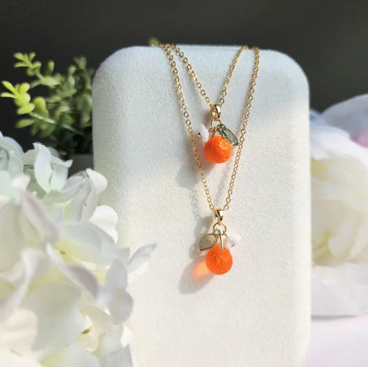 Gold necklace with orange beads on a white stand with flowers in the background