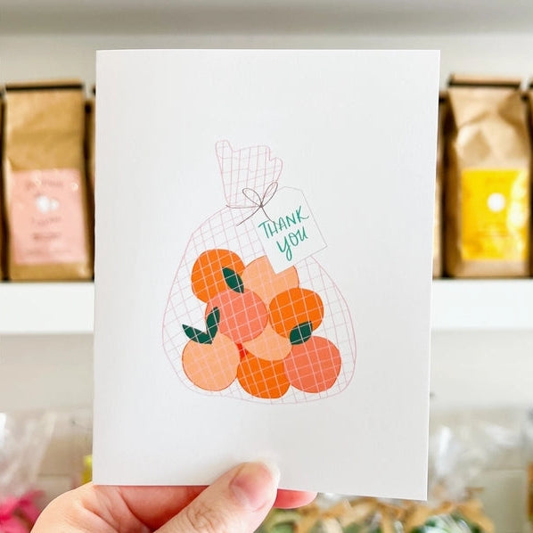 Card with a bag of oranges and 'Thank you' tag held by a hand.