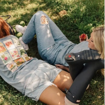 Two people sitting on grass wearing jeans with decorative patches.