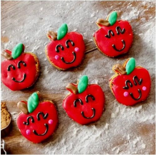 Decorative cookies shaped like red apples with smiling faces on a wooden surface.