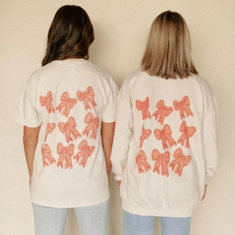 Two people wearing white t-shirts with red bow patterns on the back against a beige background.