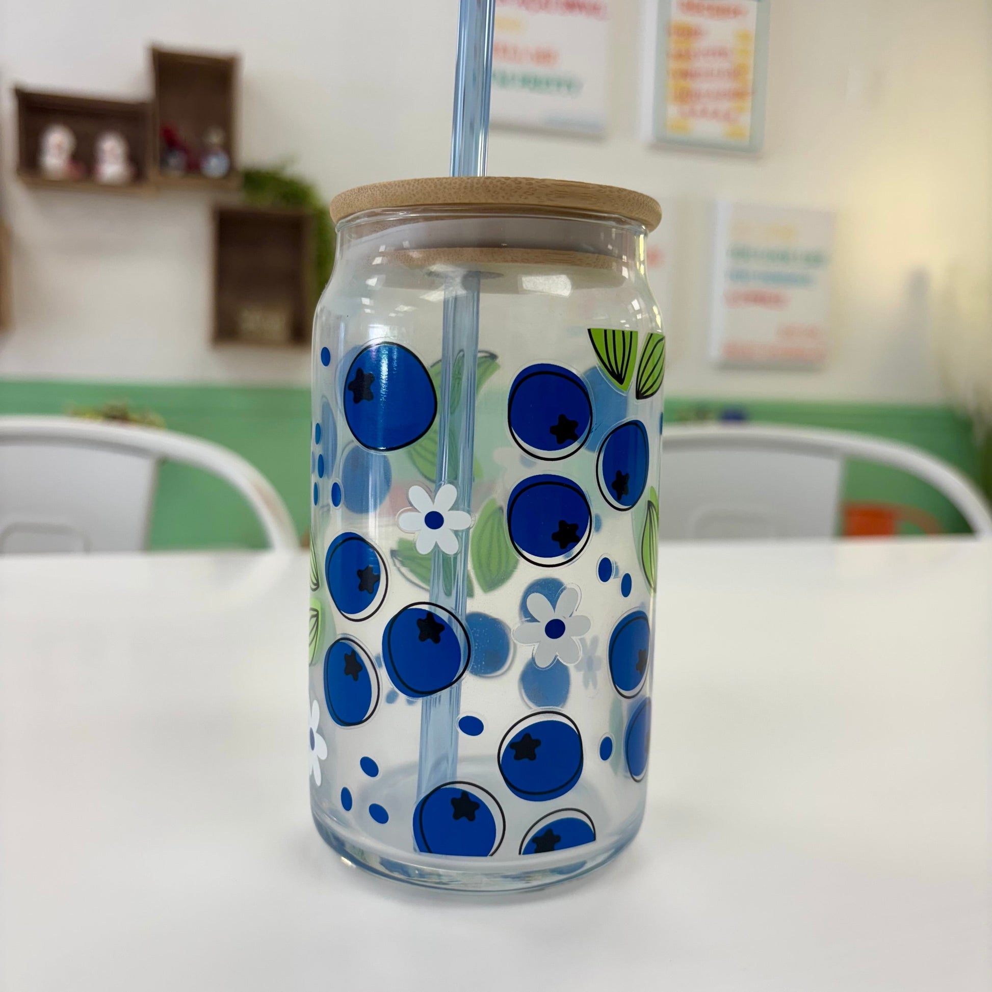 Clear glass tumbler with blue floral design, wooden lid, and straw on a white surface.