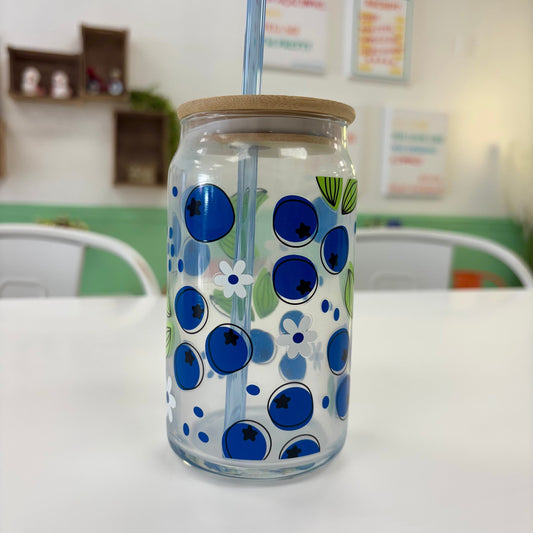 Clear glass tumbler with blue floral design, wooden lid, and straw on a white surface.