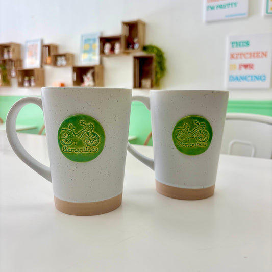 Two white mugs with green logos on a white surface, with a blurred background.