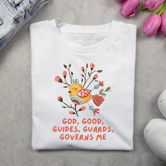 White t-shirt with a colorful bird design and text on a gray surface with flowers and denim jeans.
