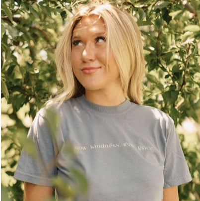 Person wearing a gray t-shirt with text, standing among trees