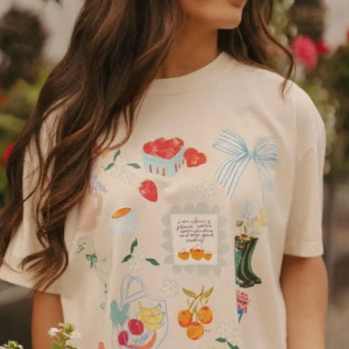 Person wearing a white t-shirt with colorful graphics and text, holding a bowl of strawberries.