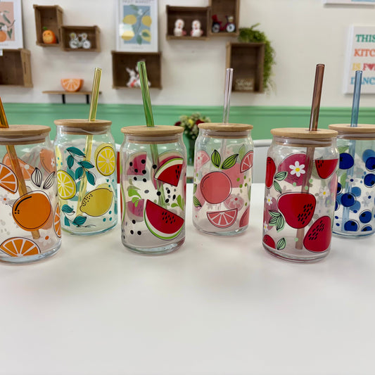 Set of glass jars with fruit designs and straws on a white surface.