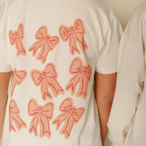 White t-shirt with pink bows on the back worn by a person.