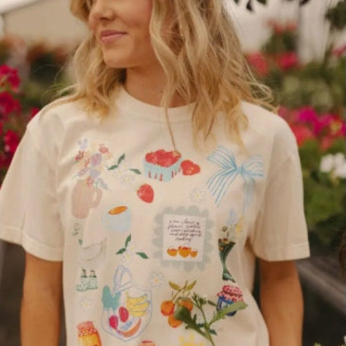 Person wearing a cream-colored t-shirt with colorful graphics, standing in a garden.