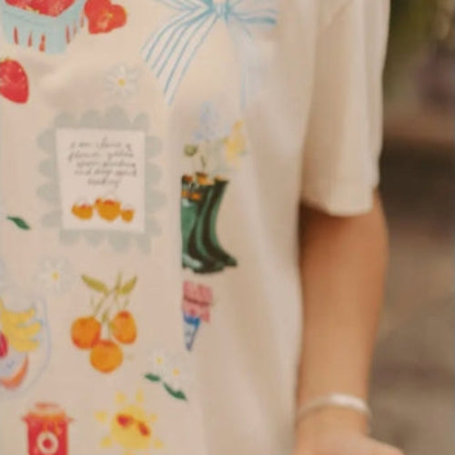 Person wearing a shirt with farm-themed illustrations holding a bowl of strawberries.
