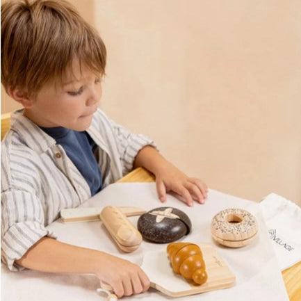 Child playing with toy bread on a tablecloth with 'Wings' branding.