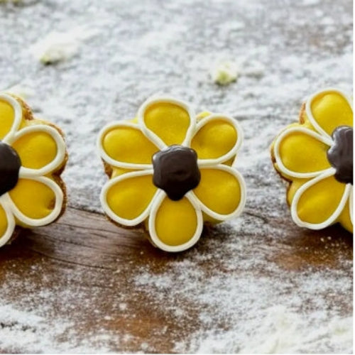 Decorative cookies shaped like flowers with yellow centers and brown stems on a wooden surface.