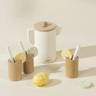 White ceramic teapot with wooden lid, wooden cups with lemon slices, and a yellow ceramic lemon on a light background.