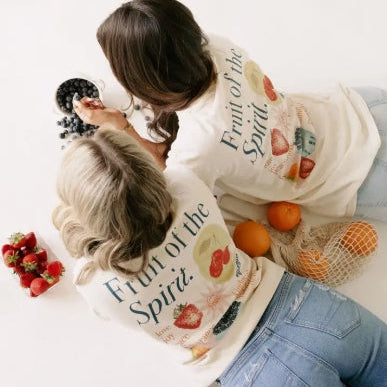 Two people wearing sweatshirts with fruit-themed designs and text, surrounded by fruits.