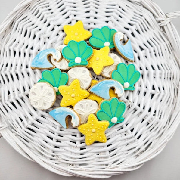 Colorful dog cookies shaped like seashells, stars, and waves on a white woven basket.