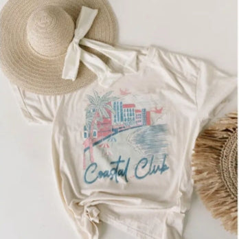 Beige t-shirt with 'Coastal Club' design, straw hat, and decorative item on a white background