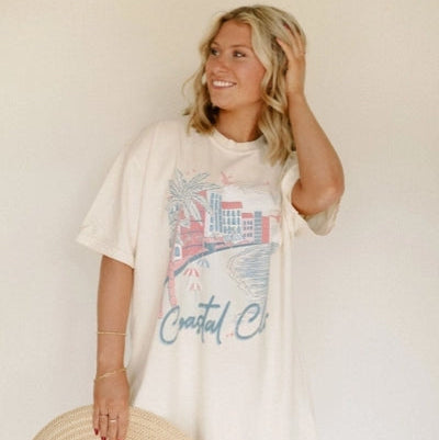 Woman wearing a white t-shirt with a graphic design and text, holding a straw hat against a plain background.