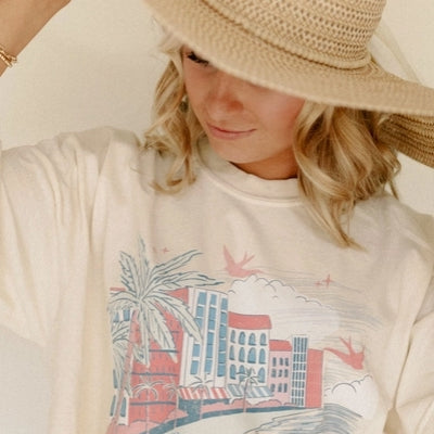 Person wearing a cream-colored t-shirt with a 'Coastal Club' graphic design.