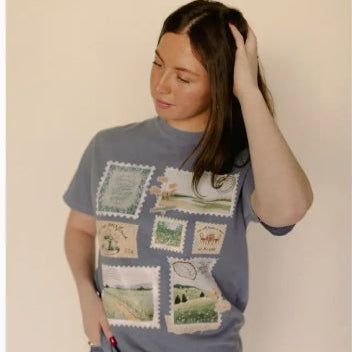 Person wearing a blue t-shirt with vintage stamp design against a plain background