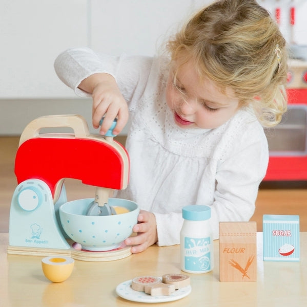 Child playing with a toy kitchen set including a mixer and various utensils on a table.