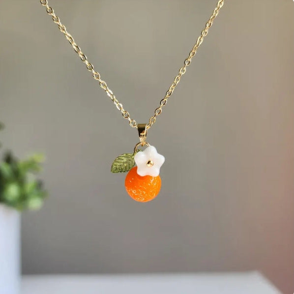 Necklace with an orange pendant and white flower on a blurred background