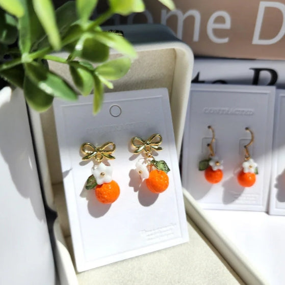 Pair of earrings with gold bows and orange fruits on a display card.