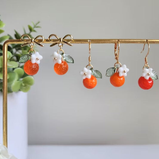 Pair of earrings with orange beads and white flowers on a gold stand.