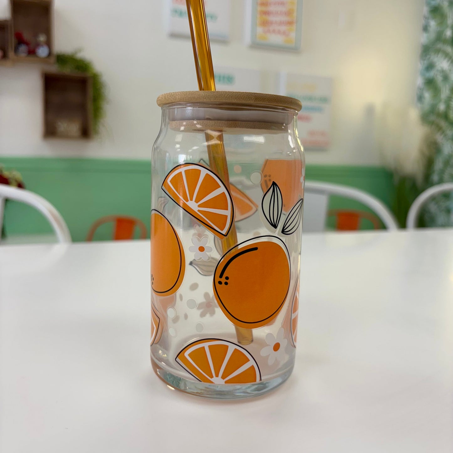 Clear glass jar with orange design and gold straw on a white surface