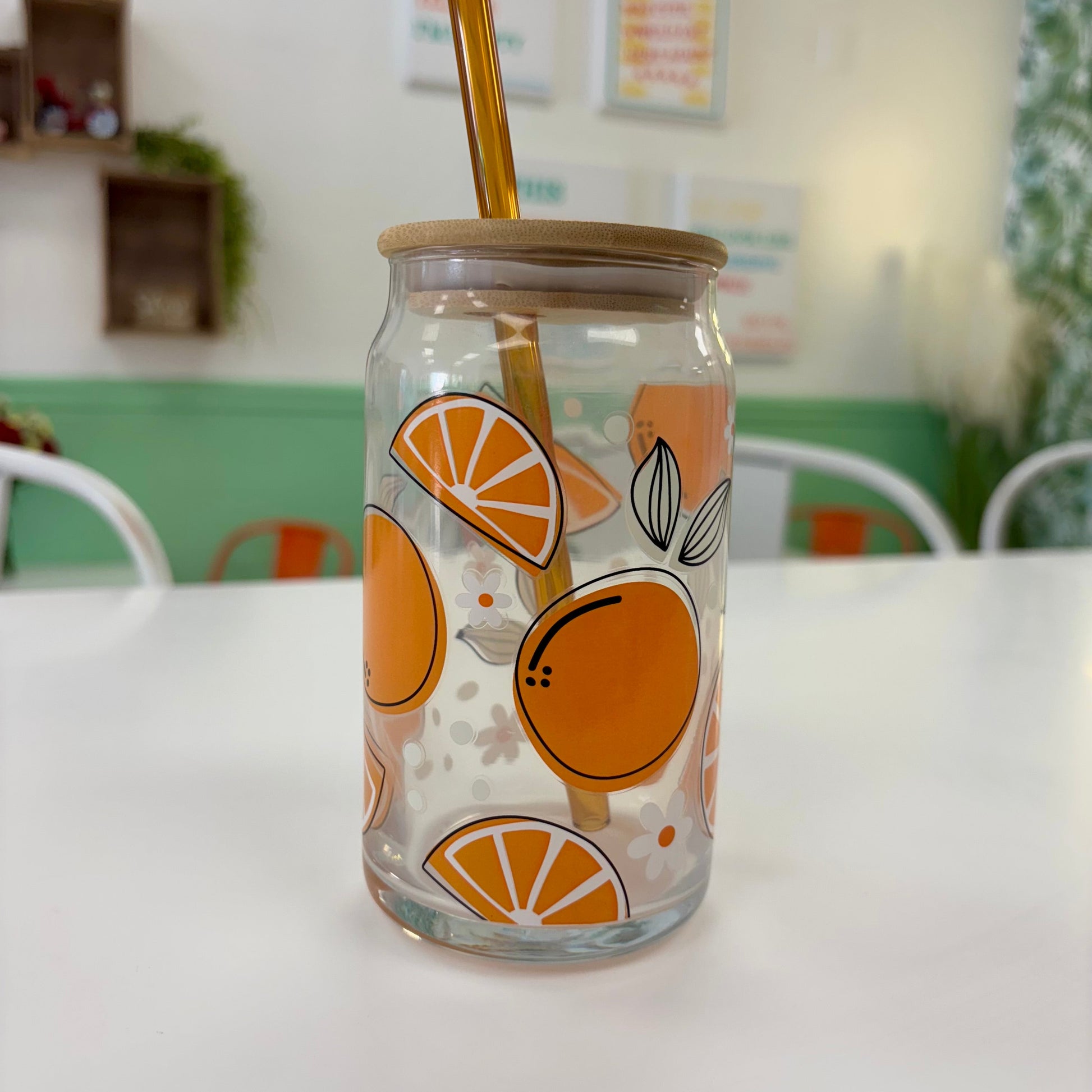 Clear glass jar with orange design and gold straw on a white surface