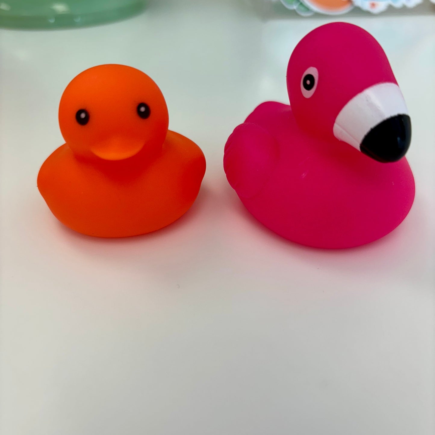 Two rubber ducks, one orange and one pink with a white beak, on a light surface.
