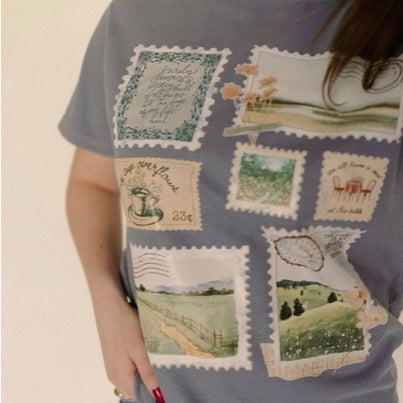 Person wearing a blue t-shirt with postage stamp designs on a beige background