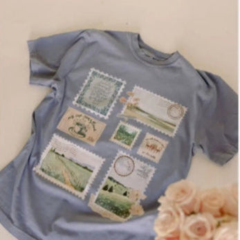 Blue t-shirt with vintage-style postage stamp designs on a light background