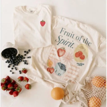 Two t-shirts with fruit-themed designs on a white surface with fruits around.