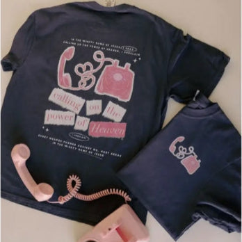 Navy blue shirt with pink phone graphic and text, placed on a light surface with a pink vintage-style phone beside it.