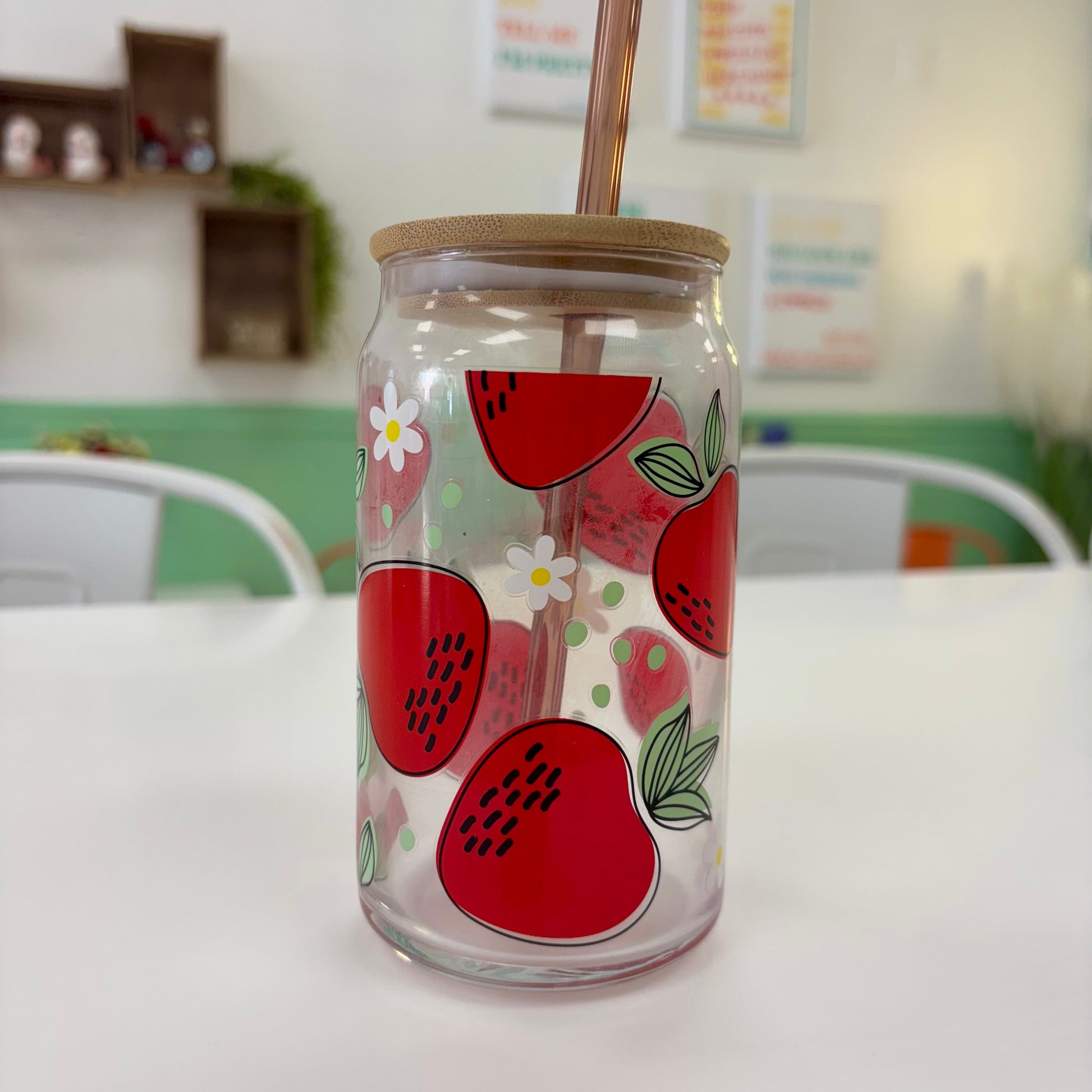 Glass jar with strawberry design and straw on a white surface