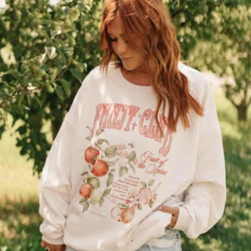 Person wearing a white sweatshirt with fruit-themed design in an outdoor setting