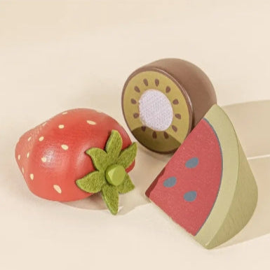 Wooden toy fruits including a strawberry, kiwi, and watermelon slice on a beige background